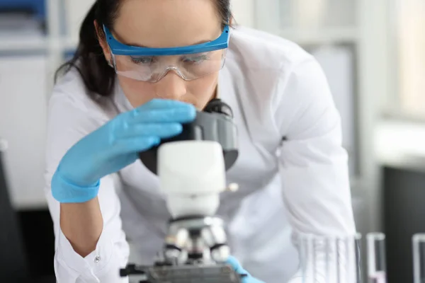 Junge Wissenschaftlerin mit Brille blickt durch Mikroskop-Nahaufnahme — Stockfoto