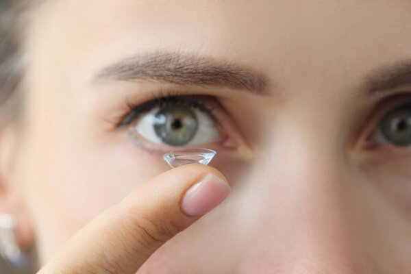 Soft contact lens on female finger against background of female eyes