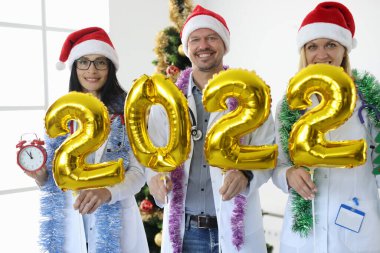 Kırmızı şapkalı doktorlar 2022 sayısını yeni yıl ağacının arka planına karşı tutuyorlar.