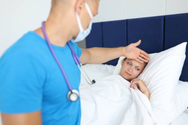 Doktor ateşli bir şekilde yatakta yatan kadının alnına el ele tutuşur.