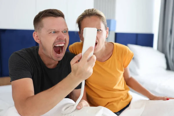 Чоловік і жінка кричать на телефонну станцію в готельному номері — стокове фото