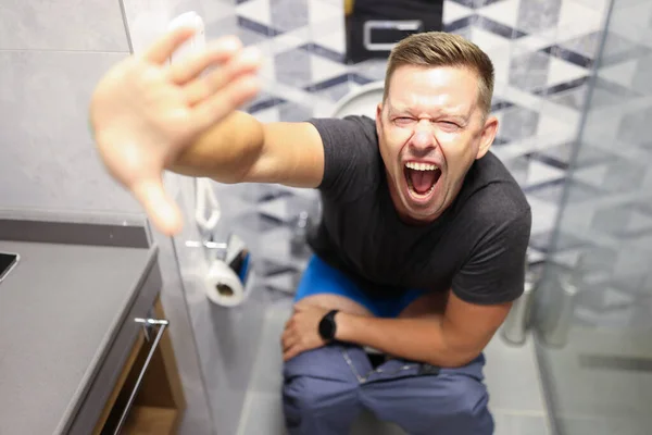 Молодий чоловік кричить, сидячи на туалеті крупним планом — стокове фото