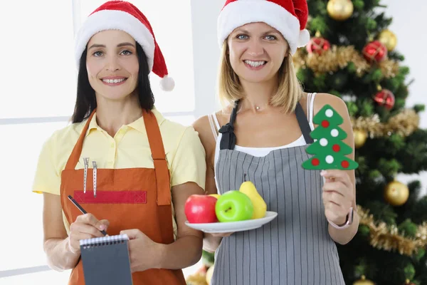 Twee lachende vrouwen serveersters op de achtergrond van Nieuwjaarsboom — Stockfoto