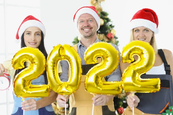 Grupo de reparadores segurando balões de hélio dourado com números 2022 perto da árvore de ano novo — Fotografia de Stock
