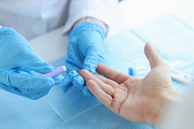 Eldiven doktoru klinikteki hastadan neşterle kan testi yaptırıyor.