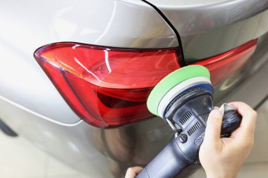 Özel makine kullanarak arabanın farlarını parlatmakta usta bir tamirci.