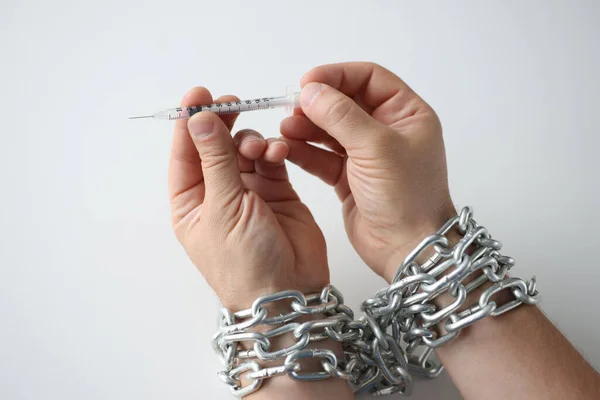 Mężczyzna z rękami związanymi metalowym łańcuchem trzymający strzykawkę z narkotykami zbliżenie — Zdjęcie stockowe