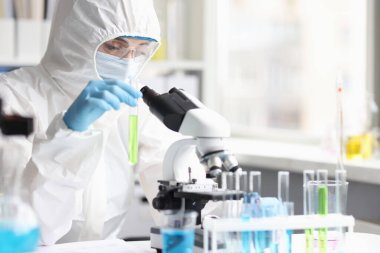 Koruyucu kıyafetli kimyager laboratuarda yeşil sıvıyla test tüpü tutuyor.