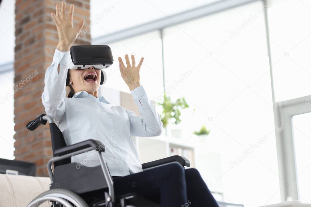 Woman sitting in wheelchair wearing virtual reality glasses and waving her hands