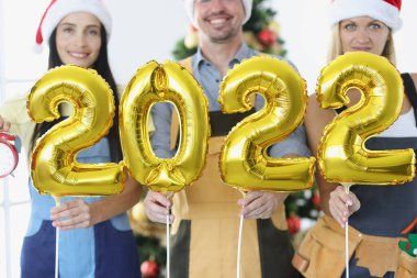 Üniformalı işçilerden oluşan gülümseyen ekip, 2022 numaralı yeni yıl ağacına karşı çıkıyor.