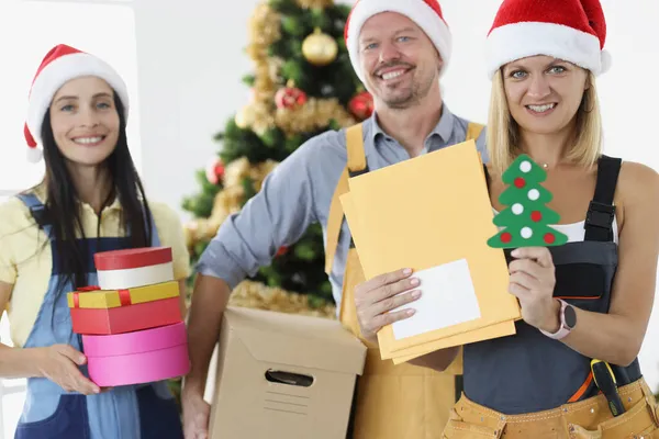 Il team di costruttori sta tenendo scatole regalo e strumenti sullo sfondo dell'albero di Capodanno — Foto Stock