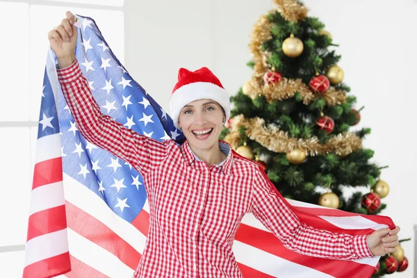 Ung leende kvinna som håller amerikansk flagga mot bakgrund av nyårsträdet — Stockfoto