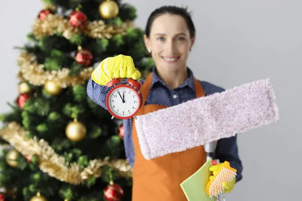 Temizlik şirketinin çalışanı yeni yıl ağacının arka planında paspas ve çalar saat tutuyor. — Stok fotoğraf