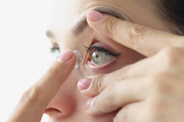 Genç bir kadın gözünün içine kontakt lens yerleştiriyor.