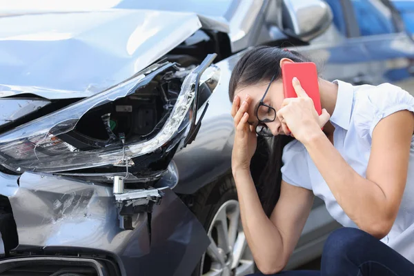 Sad woman talking on cell phone near wrecked car — Stock Photo, Image