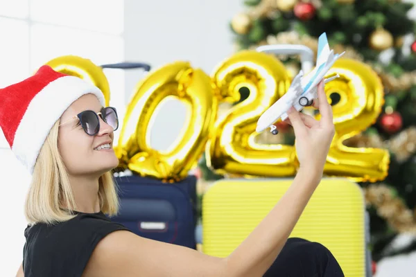 Žena v santa klobouk drží hračka letadlo v blízkosti zlatý balón s čísly 2022 a vánoční strom — Stock fotografie