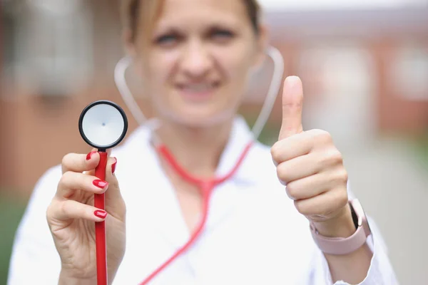 Kadın doktor baş parmağını kaldırıyor ve steteskop şefini yakın plan çekiyor. — Stok fotoğraf