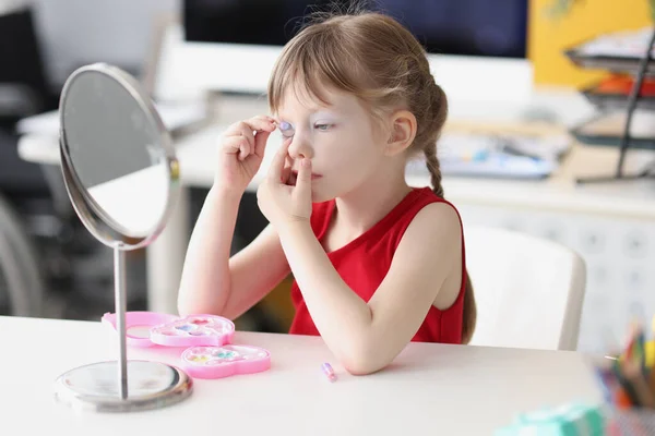 Liten flicka måla sina ögon med baby makeup framför spegeln — Stockfoto