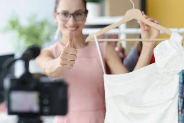 Bloggerin zeigt Daumen hoch und hält Kleid in Nahaufnahme vor der Kamera — Stockfoto