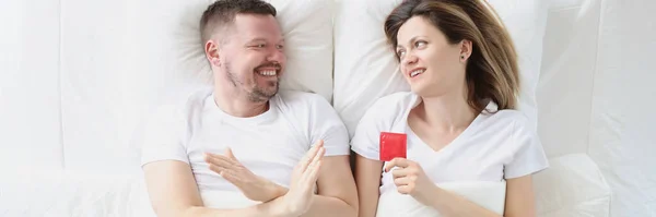 Hombre joven acostado en la cama con la mujer y rechazando el condón vista superior — Foto de Stock