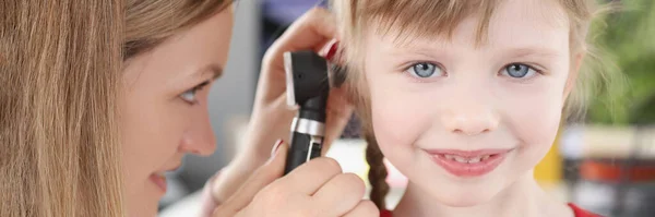 Woman pediatrician looking at eardrum of little girl using otoscope in clinic — Stock Photo, Image