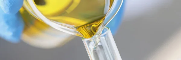 Chimist om de știință turnarea de ulei galben din borcan de sticlă în closeup tub de testare — Fotografie, imagine de stoc