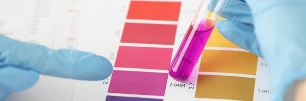Wissenschaftler vergleicht lila Flüssigkeit im Reagenzglas mit Farbbalken — Stockfoto