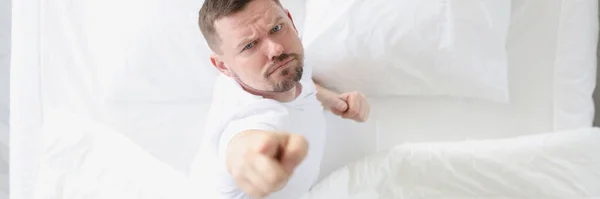 Hombre joven acostado en la cama blanca y mostrando el dedo índice arriba de la vista superior —  Fotos de Stock