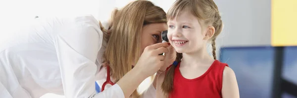Woman pediatrician examining ear of little girl with otoscope at clinic — ストック写真
