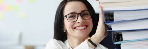 Junge Frau mit Brille hält viele Ordner mit Dokumenten im Büro — Stockfoto