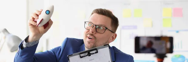 Emotional male blogger holds rocket in hand and conducts online training on quick start in business — Stock Photo, Image