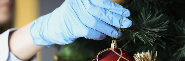 Frau in Schutzhandschuhen hängt Silvesterball am Weihnachtsbaum — Stockfoto
