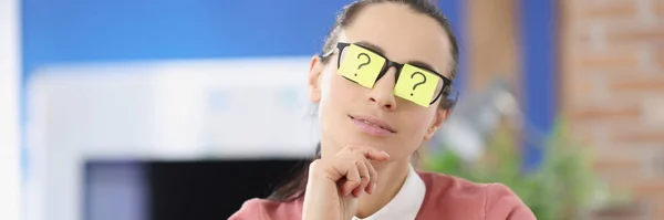 Молода жінка з наклейками з позначкою питання на окулярах сидить в офісі — стокове фото