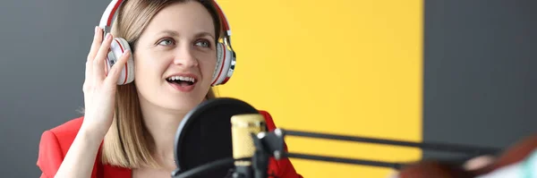 Mulher cantora em fones de ouvido cantando música em microfone em estúdio de gravação — Fotografia de Stock