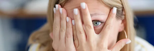 Mujer cubre la cara con su mano mirando a través de los dedos de cerca —  Fotos de Stock