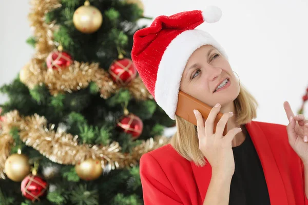 Biznesmen rozmawia przez telefon w Santa Claus kapelusz na tle Nowego Roku drzewa — Zdjęcie stockowe