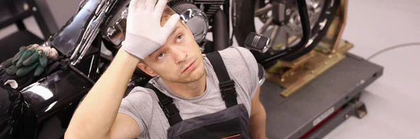 Maestro reparador cansado sentado cerca de la motocicleta y sosteniendo su cabeza en el taller — Foto de Stock