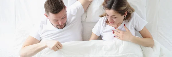Yatakta yatarken battaniyenin altına bakan neşeli bir adam ve kadın. — Stok fotoğraf