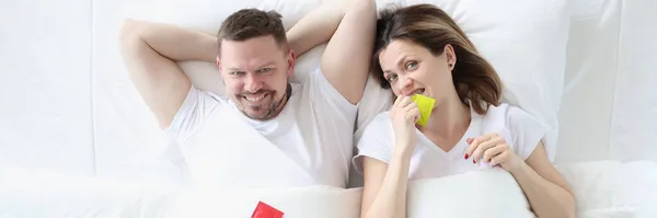 Hombre feliz mujer se acuesta en la cama con condones —  Fotos de Stock