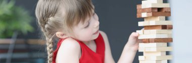 Girl plays and takes out wooden blocks from tower