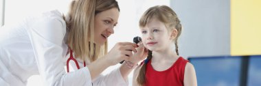 Doktor küçük bir kızın kulağını muayene ediyor.