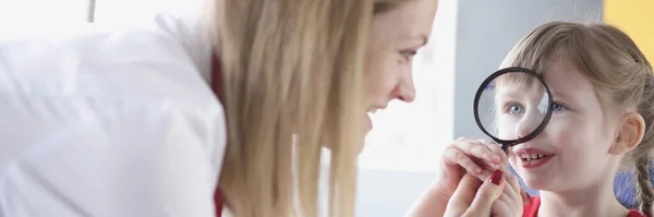 Little girl looks through magnifying glass at doctor closeup — 스톡 사진