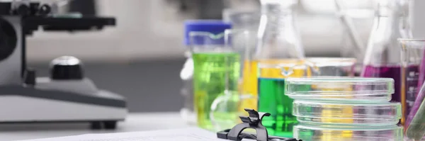 Microscope multicolored liquid in test tubes and papers on table in laboratory — Fotografia de Stock