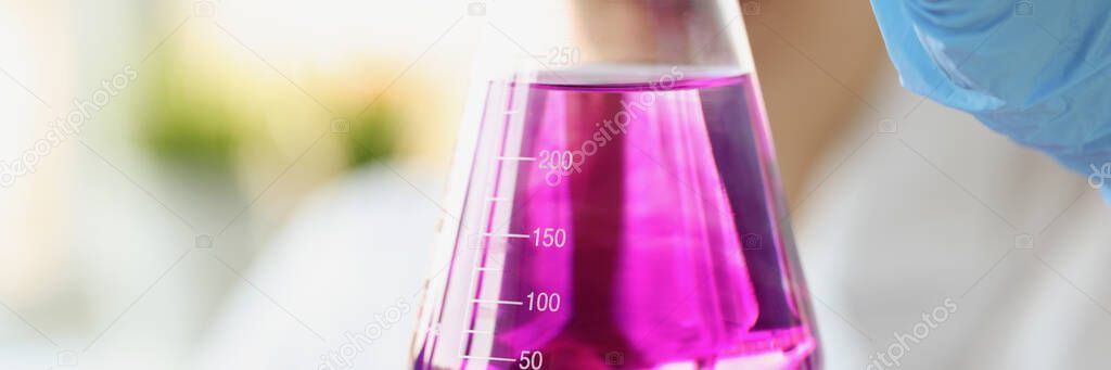 Researcher holds flask of purple liquid with gloves