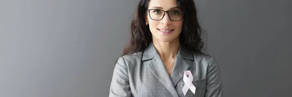 Ritratto di donna sorridente in abito grigio sul petto con nastro rosa simbolo di lotta contro il cancro al seno — Foto Stock