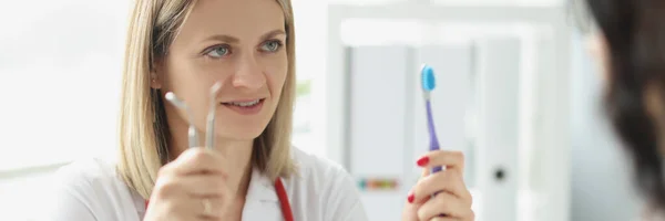 Mujer doctor dentista muestra paciente cepillo de dientes e instrumento dental —  Fotos de Stock