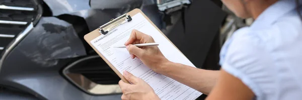 Woman insurance agent filling out paperwork near wrecked car closeup — Stock Photo, Image