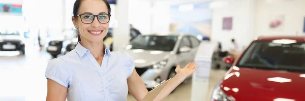 Жінка продавець з буфера в руках показує нову машину в дилерському центрі — стокове фото