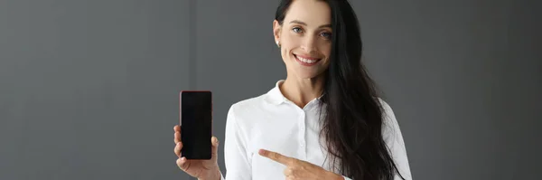 Junge Frau hält Handy in der Hand und zeigt mit Zeigefinger darauf — Stockfoto