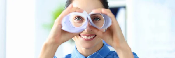 Glimlachende vrouw kijkt door verrekijker gemaakt van papier closeup — Stockfoto